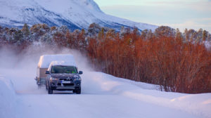 Car (SUV) moving on snowy road with small trailer at the winter